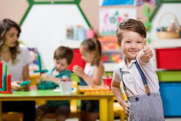 Kindergartenkind lächelt in die Kamera und zeigt einen Daumen hoch